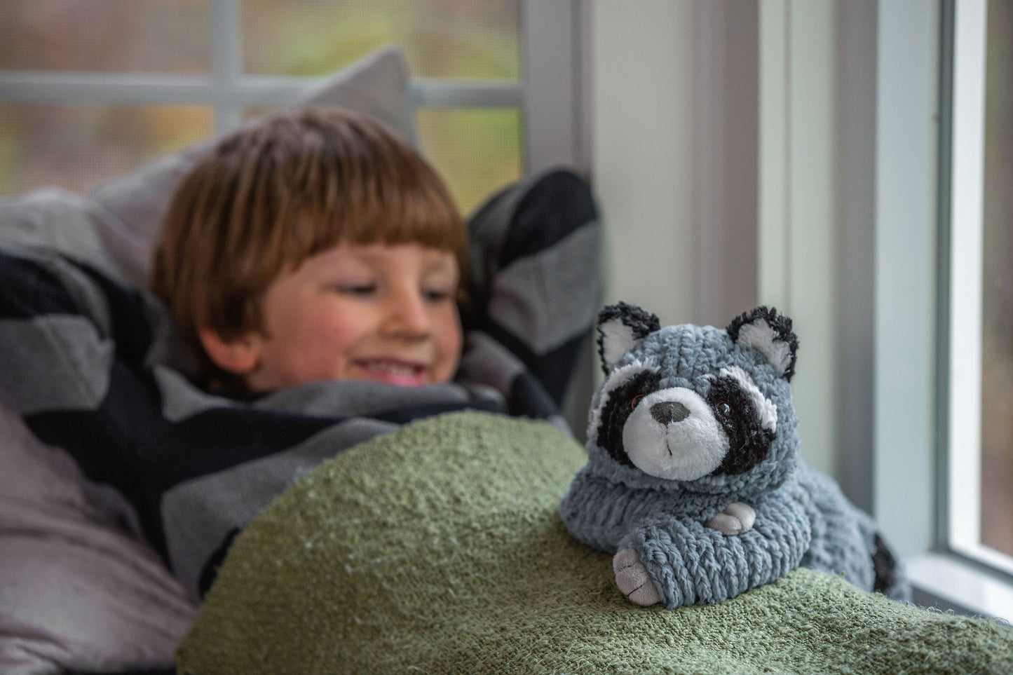 Child lying on a bed with a raccoon plush toy next to them