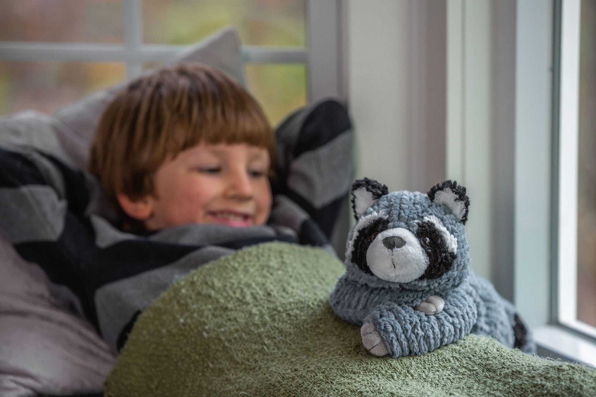 Child lying on a bed with a raccoon plush toy next to them