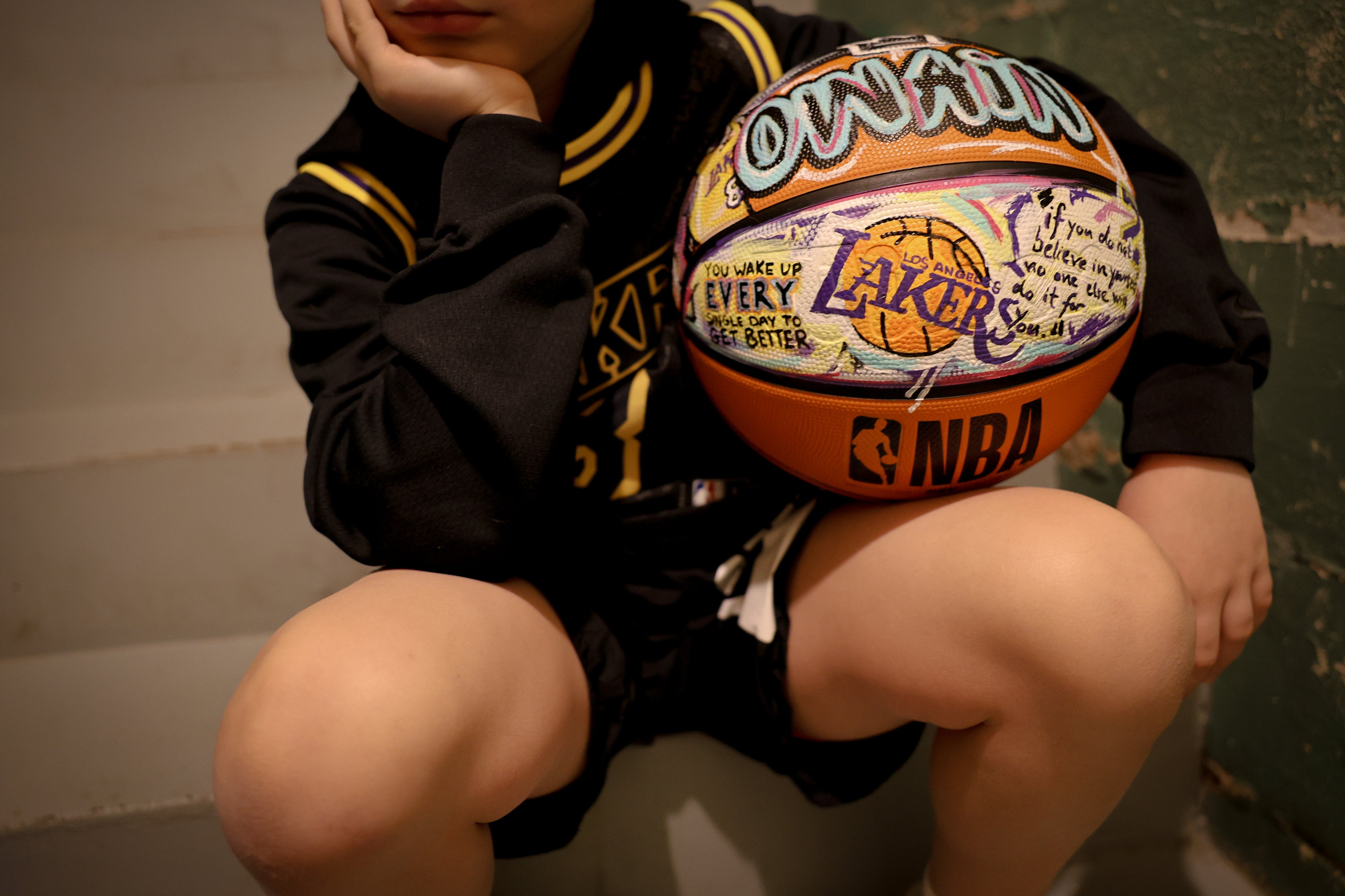 Person holding a Lakers basketball with text on it, sitting against a plain background